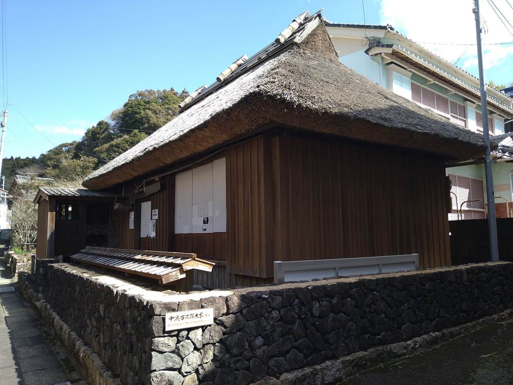 ジョン万次郎生家(復元)の外観。石垣に「中浜万次郎生家(復元)」の看板と、集落の路地